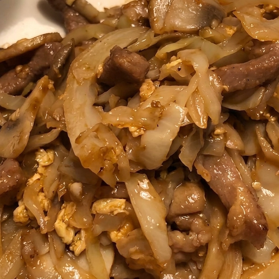 Close-up of sautéed beef with onions and scrambled egg pieces on a white plate.